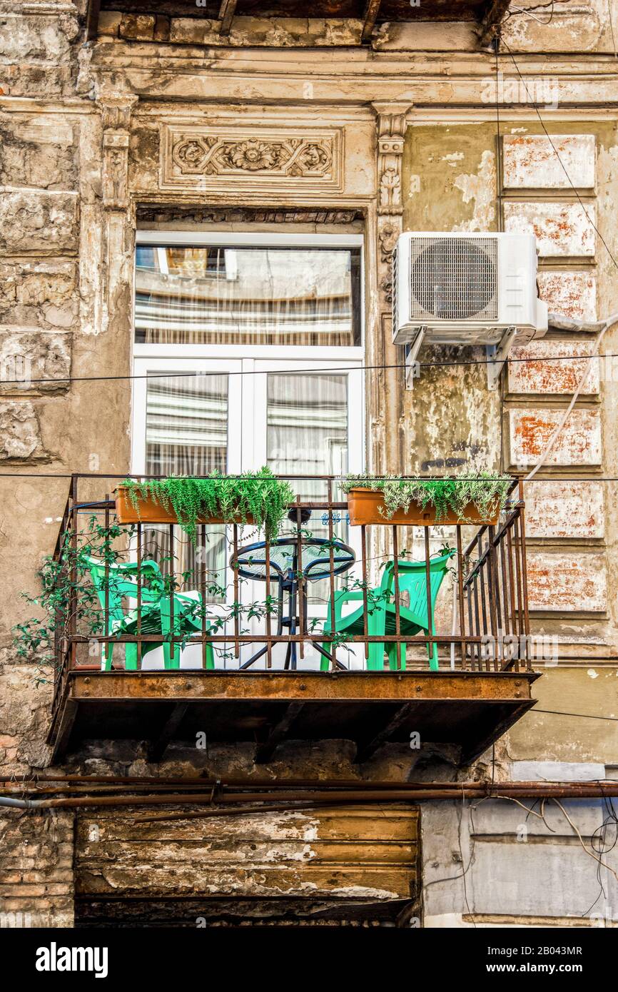 Balcone urbano - bellissima grunge - balcone arrugginito fuori dal vecchio edificio europeo con piante e sedie in plastica sotto portale scolpito con unità ac a s. Foto Stock