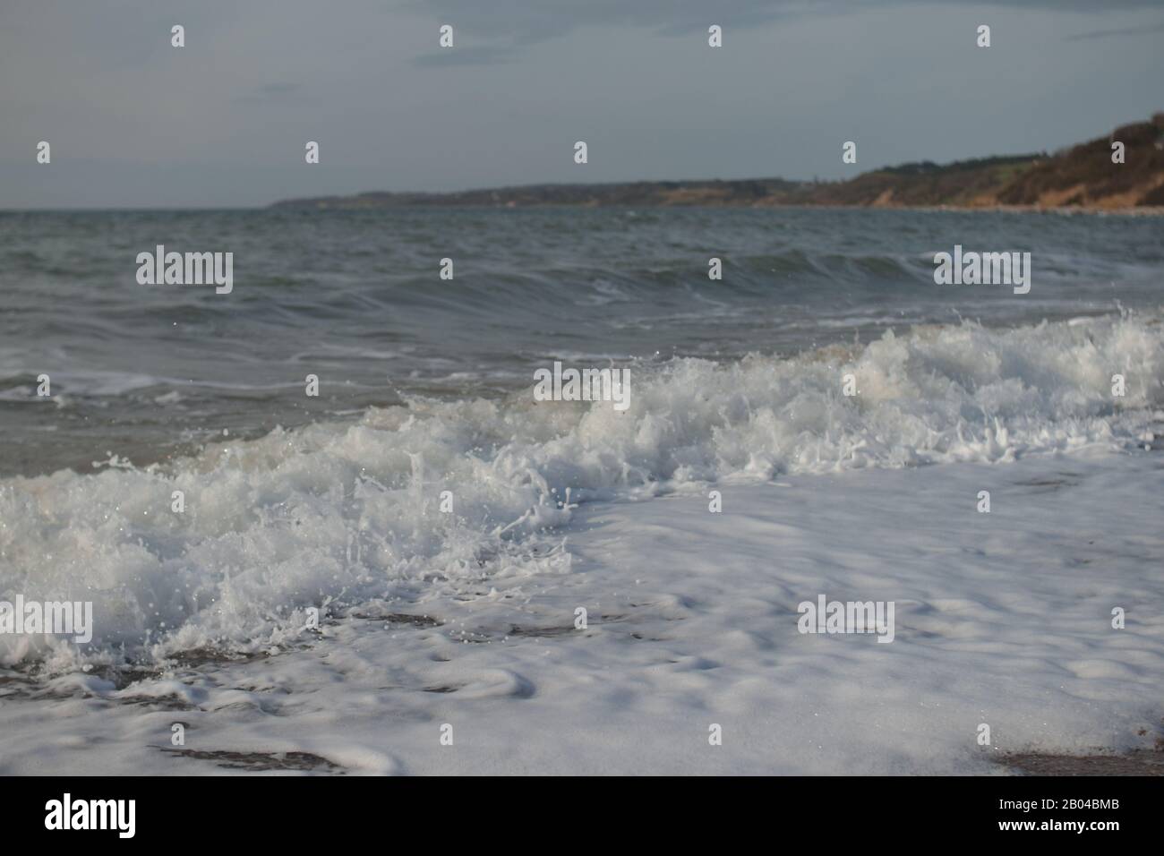 onde schiumose che scheggiano sulla costa con scogliere sullo sfondo a kaldundborg Foto Stock