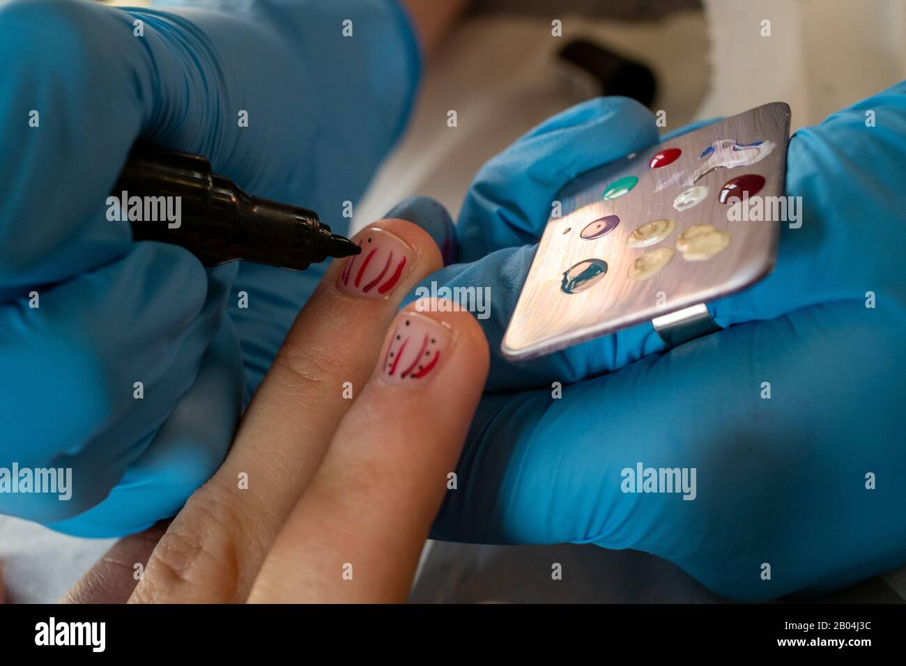 Primo piano di nail artist aggiungendo punti al disegno sulle unghie delle dita corte della giovane donna. Foto Stock