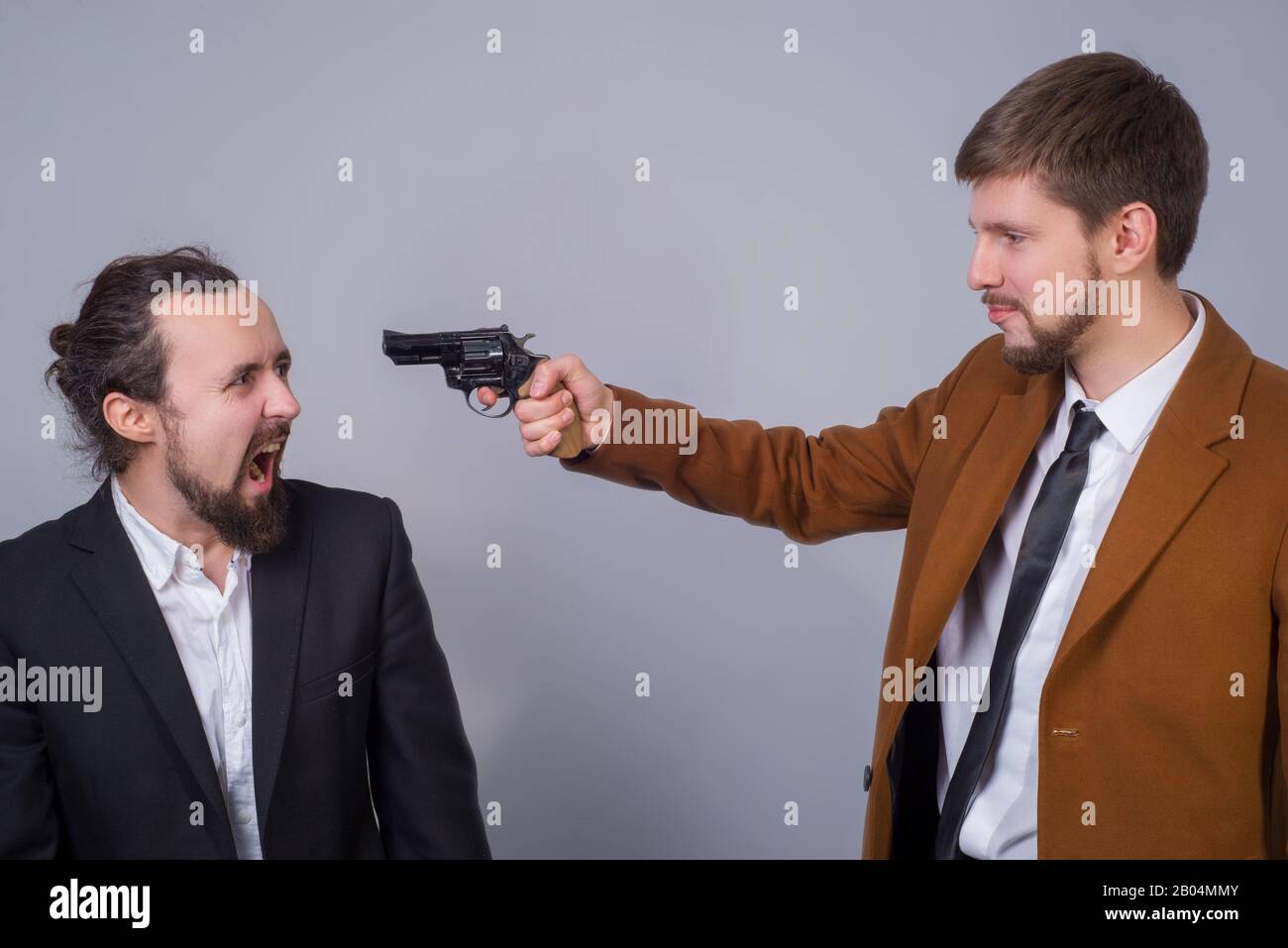 Ritratto di due giovani in abiti da lavoro. L'uomo punta la pistola ad un altro uomo, minacciandolo, e il secondo lo guarda in fright e scre Foto Stock
