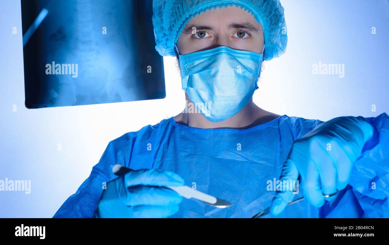 Ritratto di un chirurgo in abiti sterili, cappelli e maschere. Tenendo un bisturi e un supporto dell'ago con un ago, indirizzarli nella ferita chirurgica, p. Foto Stock