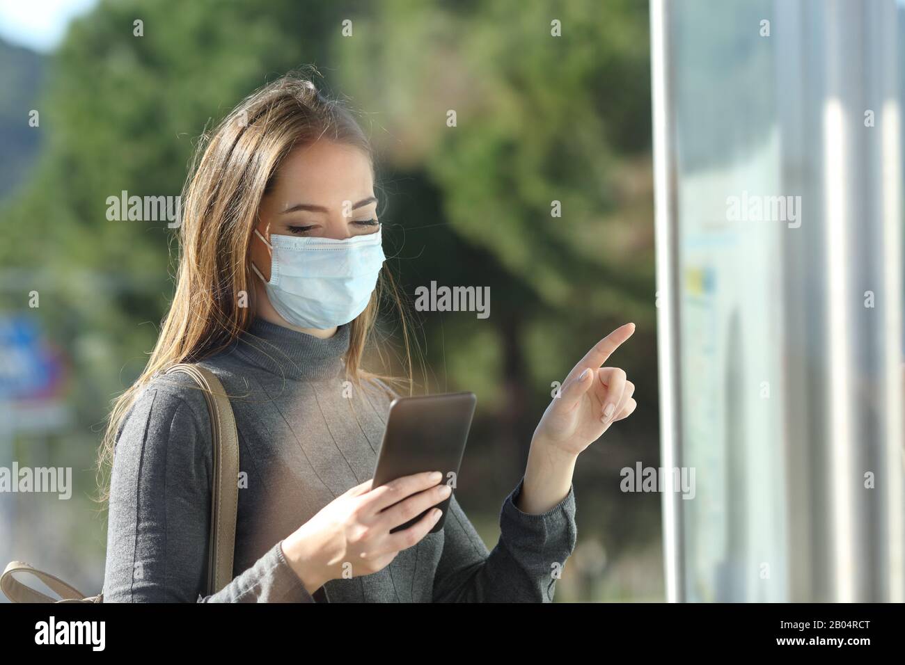 Pendolari con una maschera protettiva che evita il contagio controllando il programma del bus Foto Stock