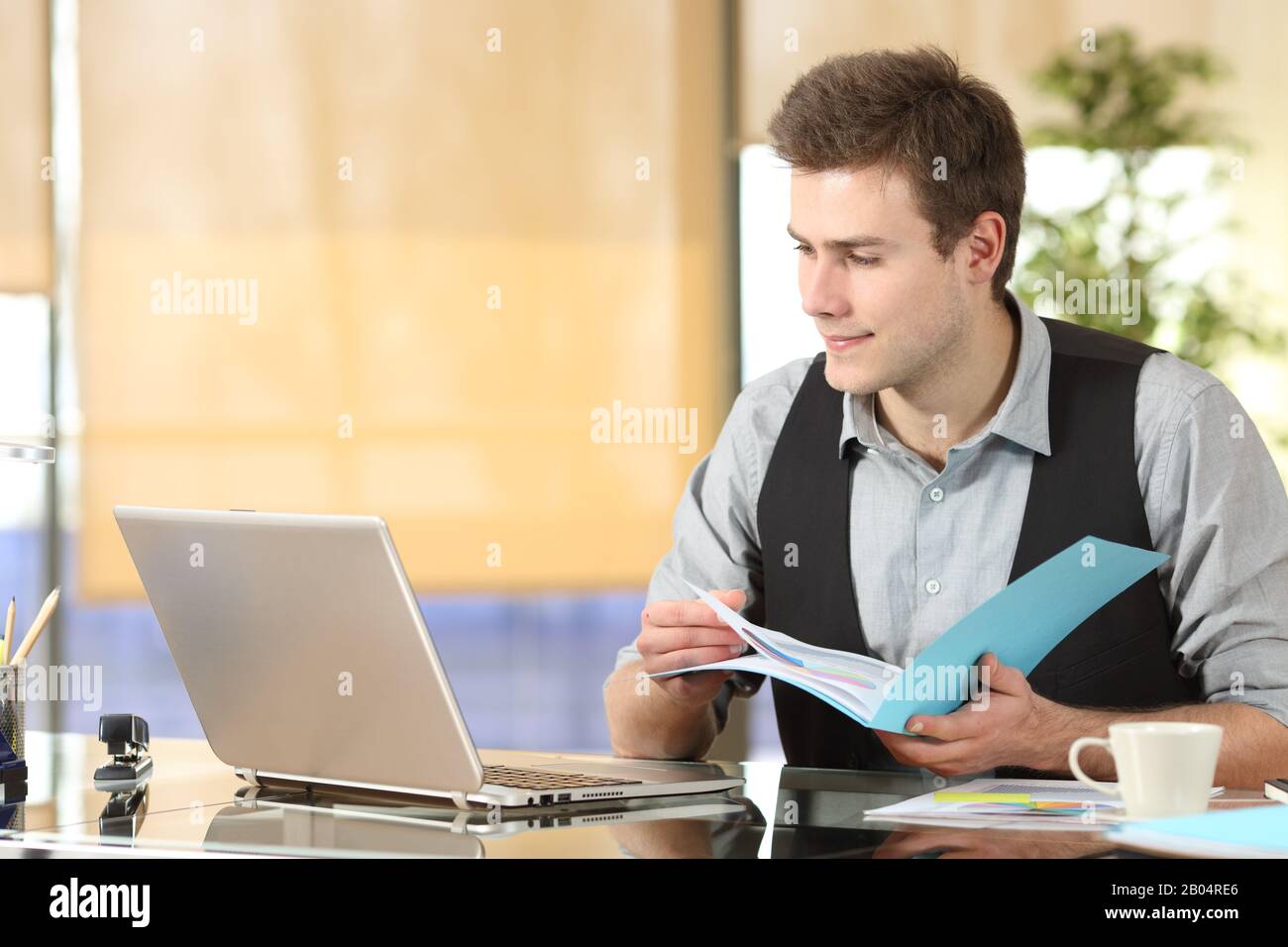 Lavoratore serio che confronta i contenuti online dei notebook e i documenti cartacei in ufficio Foto Stock