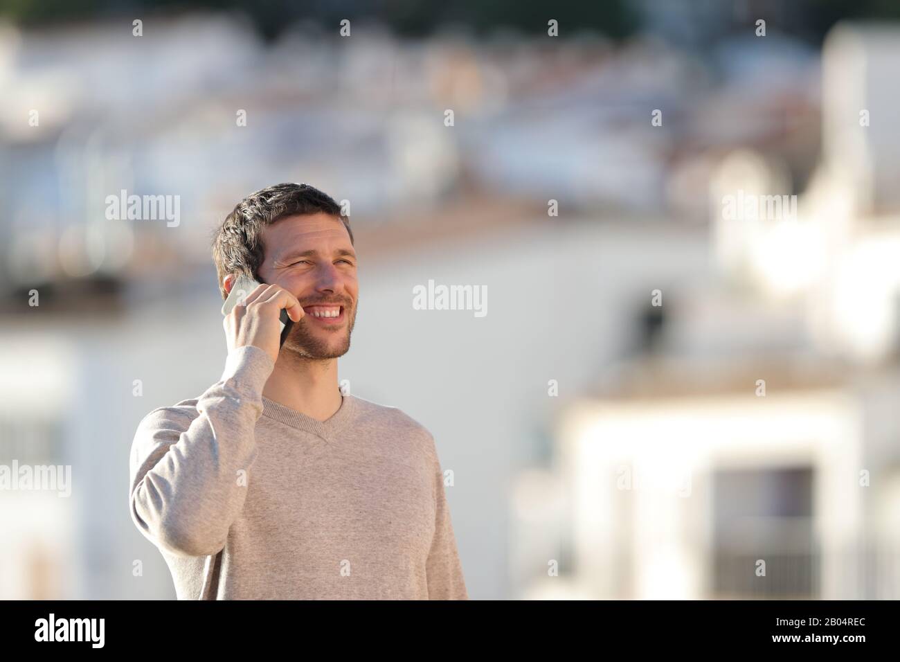 Uomo felice che parla sul telefono cellulare a piedi in una città rurale Foto Stock