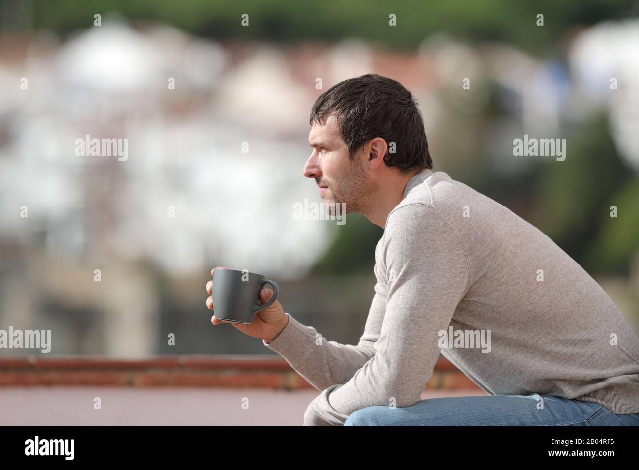 Vista laterale ritratto di un uomo serio seduto su una panchina che tiene la tazza del caffè contemplando le viste in una città Foto Stock