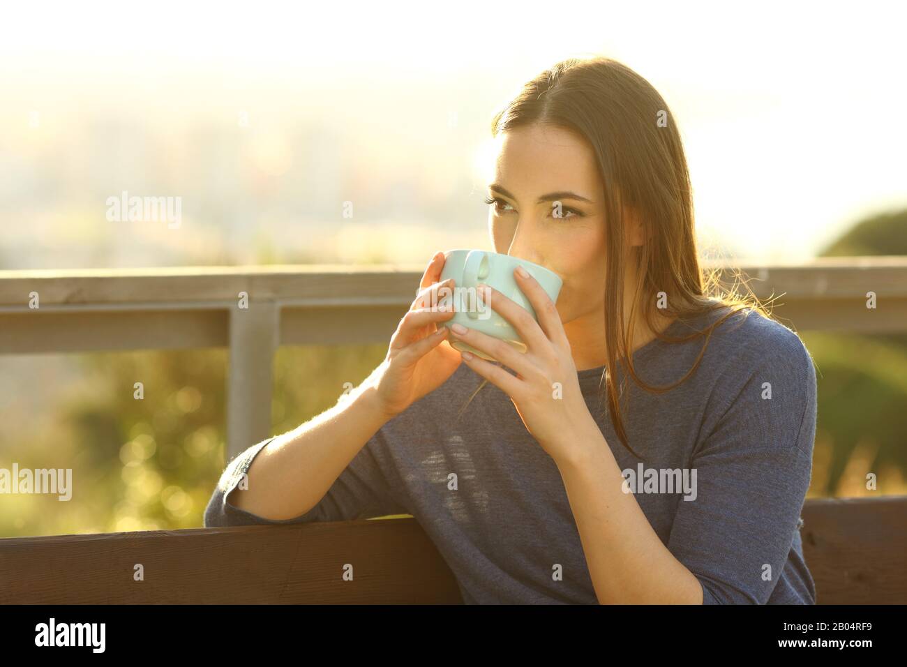 Donna rilassata bevendo caffè seduto su una panchina in un parco al tramonto Foto Stock