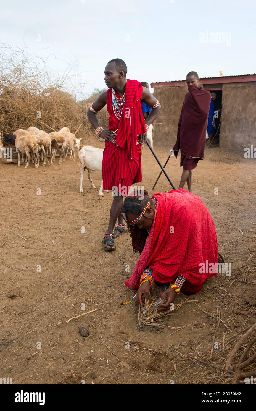 Scena del villaggio con uomini Masai che fanno un fuoco il modo tradizionale con un bastone di legno e frizione in un villaggio Masai fuori del Parco Nazionale Amboseli in K Foto Stock