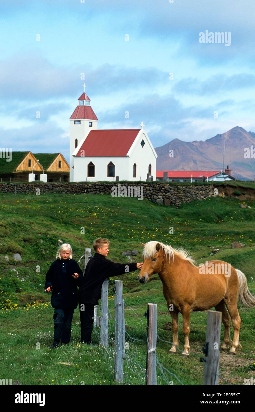 ISLANDA, PARTE ORIENTALE, MODRUDALUR, CAVALLO ISLANDESE, BAMBINI, CHIESA SULLO SFONDO Foto Stock
