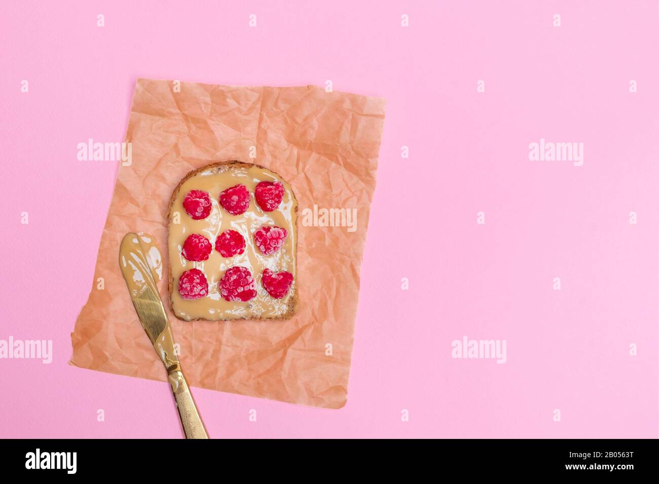 Toast al burro di arachidi con lamponi su sfondo rosa pastello. Immagine con spazio di copia, vista dall'alto Foto Stock