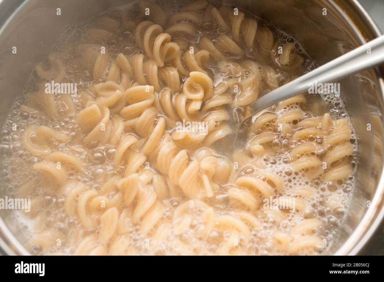 Pasta a grani interi in una padella con acqua bollente e un cucchiaio. Cucinare cibo sano Foto Stock