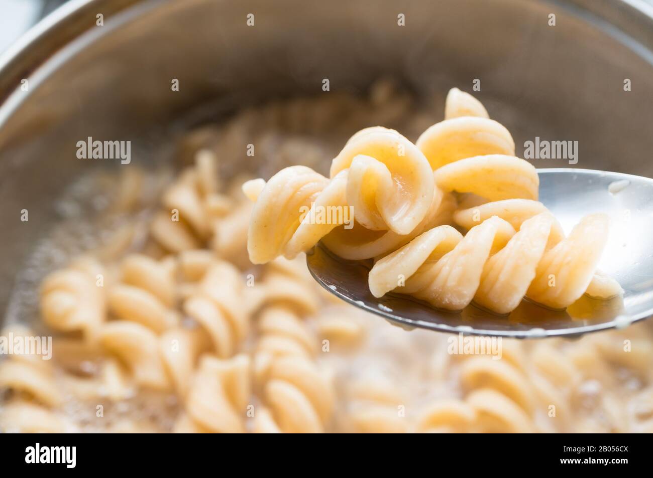 Un cucchiaio con fusilli di grano intero su un fondo di pasta, cucinato in una pentola. Mangiare sano. Foto Stock