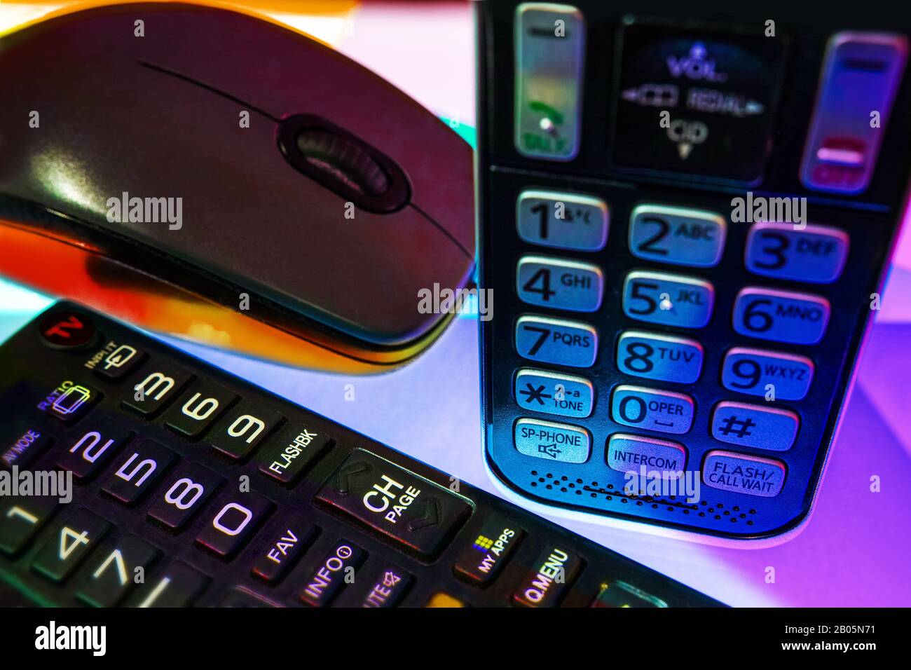 Su una superficie multi-colorata vediamo un telecomando TV, un mouse per computer e un telefono. Foto Stock