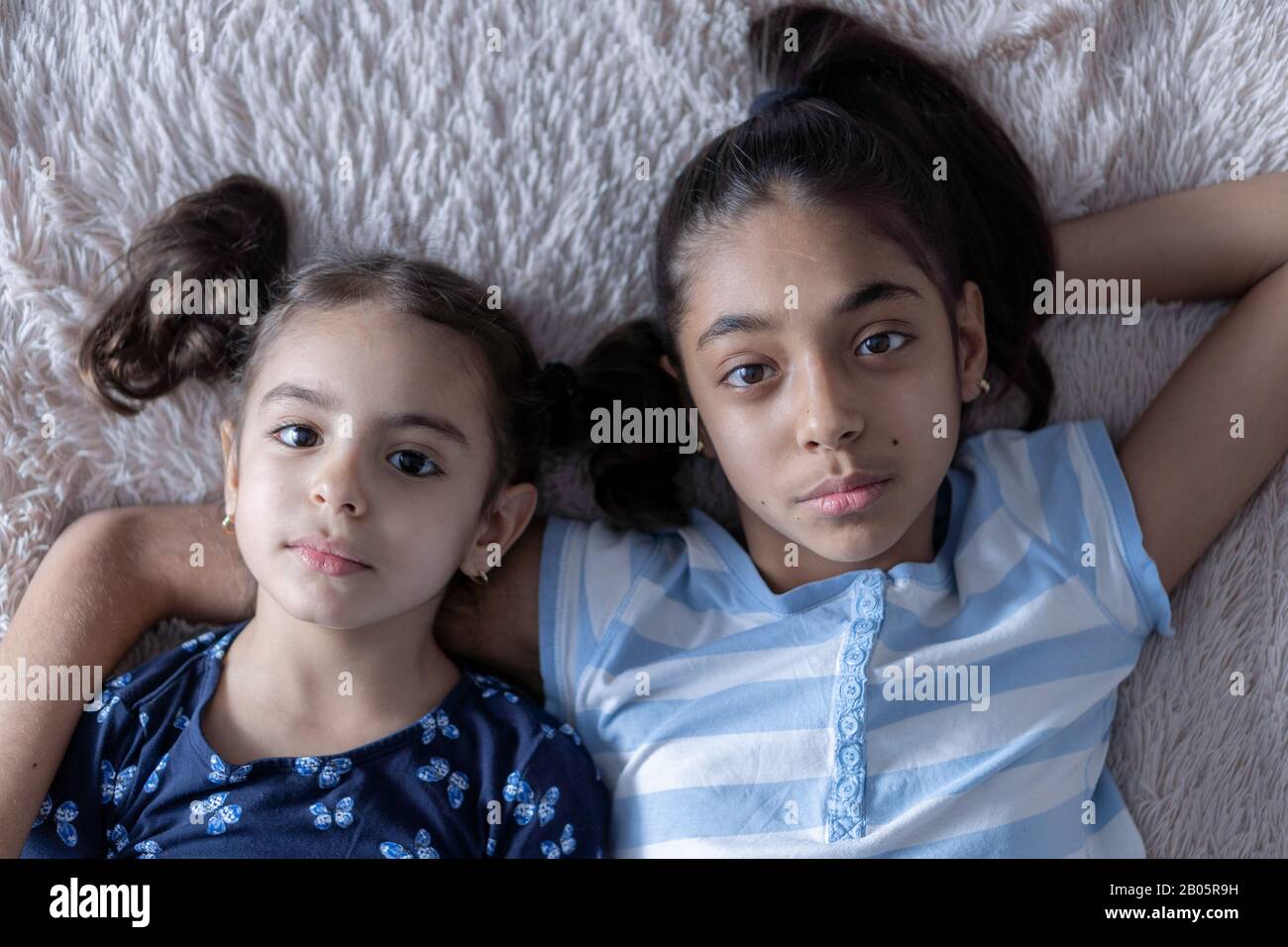Due ragazze nere, sorelle, si trovano a letto in un abbraccio alle spalle. Ragazze persiane sul letto con un telefono. Bambini del Medio Oriente. Foto Stock