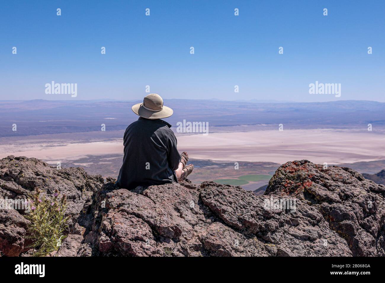 Una giovane donna in un cappello di paglia seduto su una scogliera che si affaccia sul deserto di Alvord. Steens Mountains, Oregon Meridionale Foto Stock