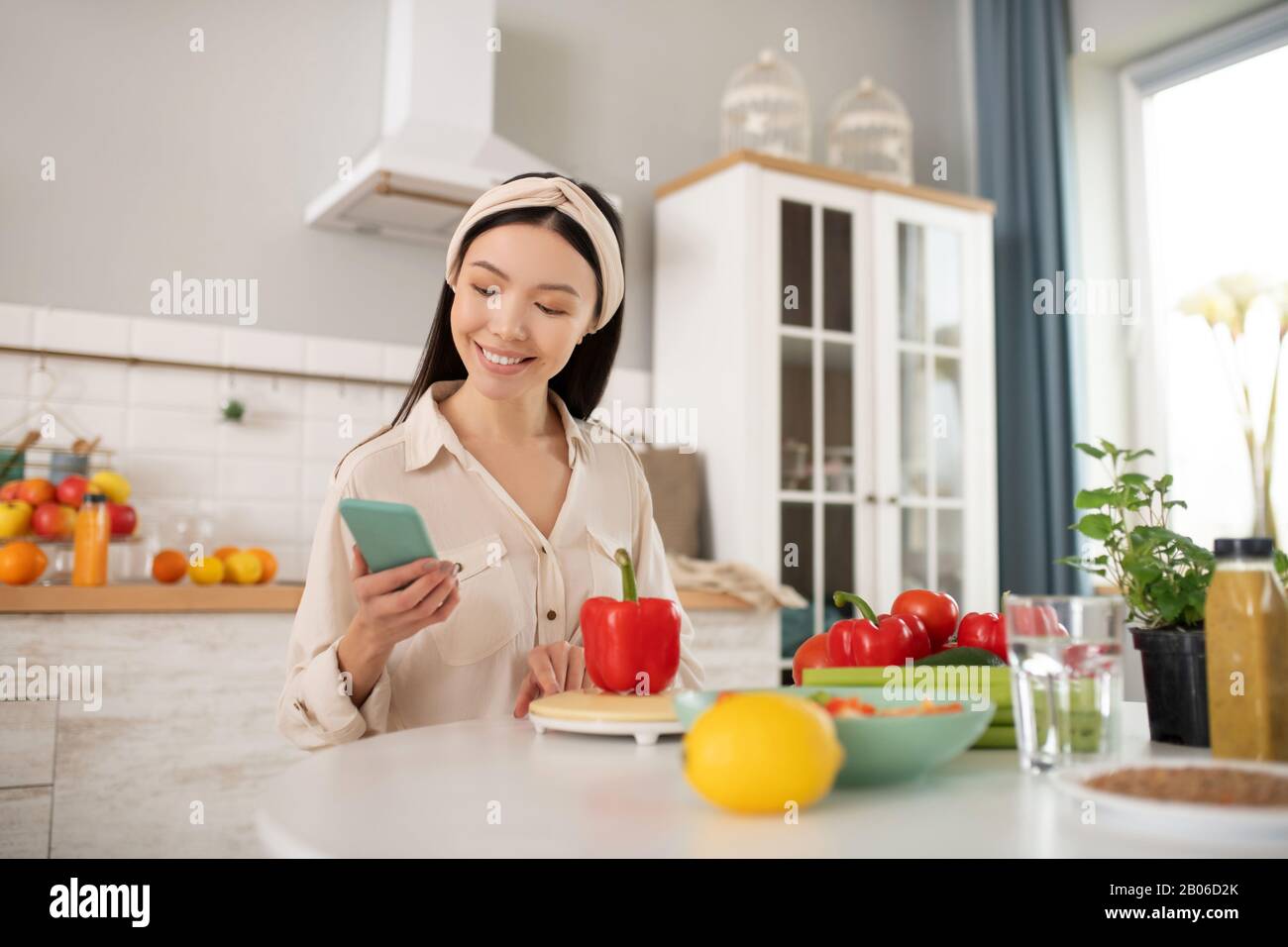 Ragazza carina con smartphone in mano seduto in cucina. Foto Stock
