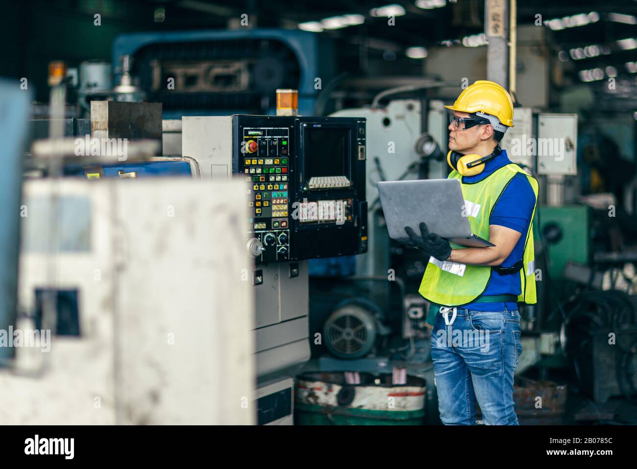 Il tecnico asiatico ha programmato la macchina in fabbrica con un computer portatile per configurare il processo di programmazione. Foto Stock