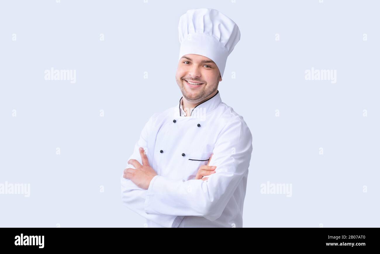 Uomo Chef In Piedi Crossing Mani Sorridenti A Fotocamera, Studio Shot Foto Stock