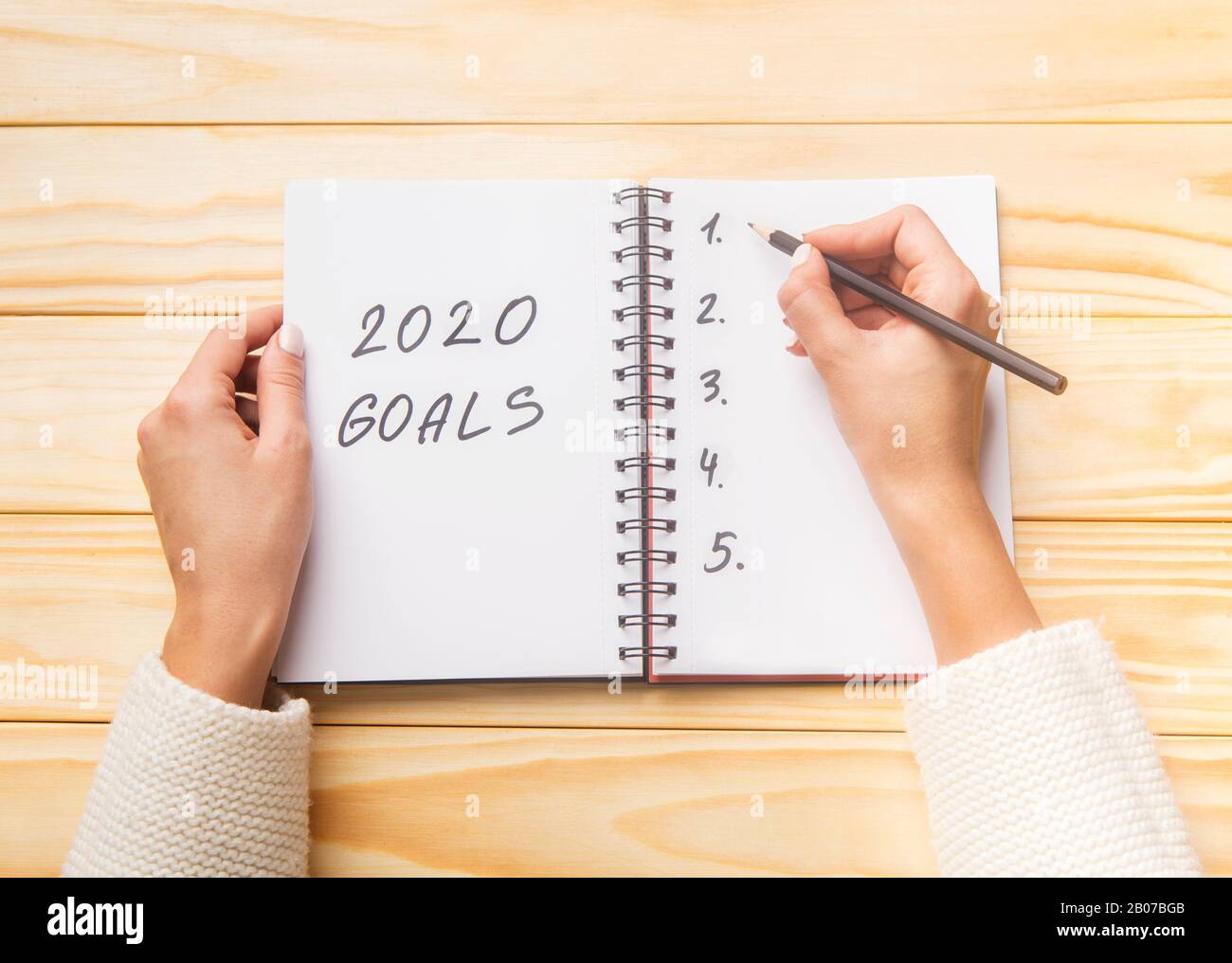 Mani femminili che scrivono gli obiettivi futuri 2020 in blocco note a spirale Foto Stock