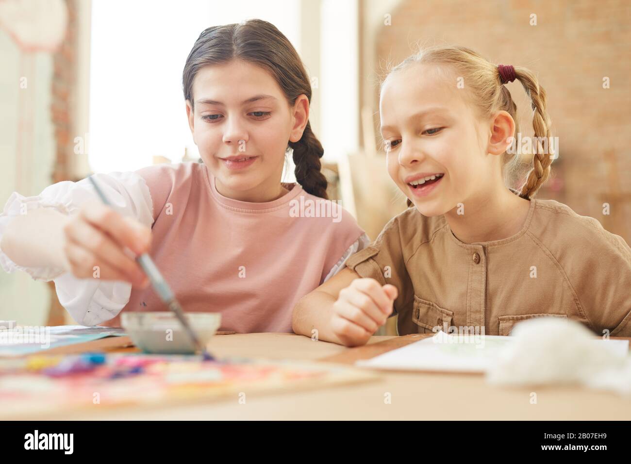 Due amici felici seduti al tavolo e dipingere un quadro insieme con le pitture a scuola Foto Stock