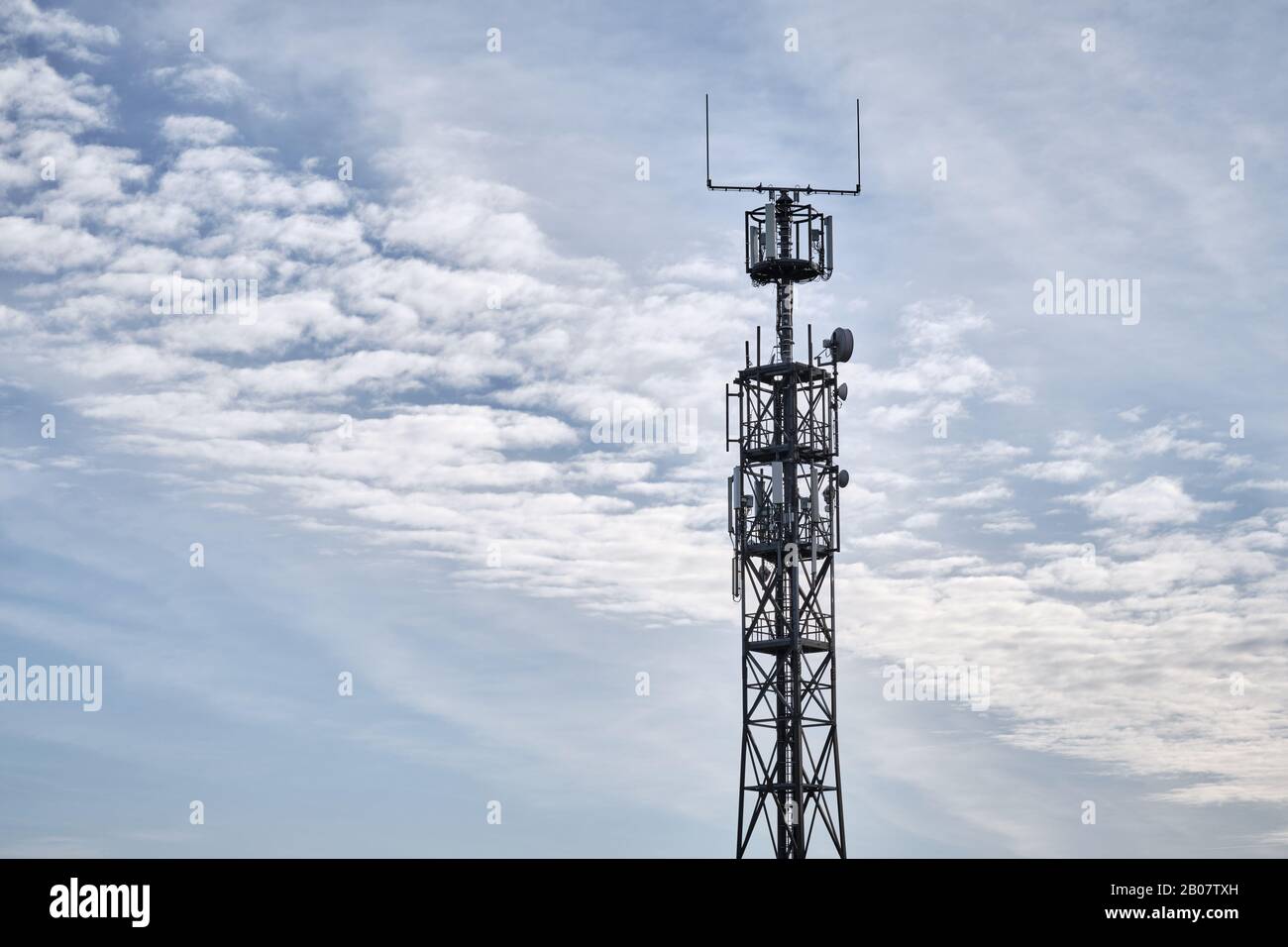 Primo piano di traliccio con stazione base per comunicazioni mobili contro cielo blu con nuvole. Visto in Germania nel mese di febbraio Foto Stock