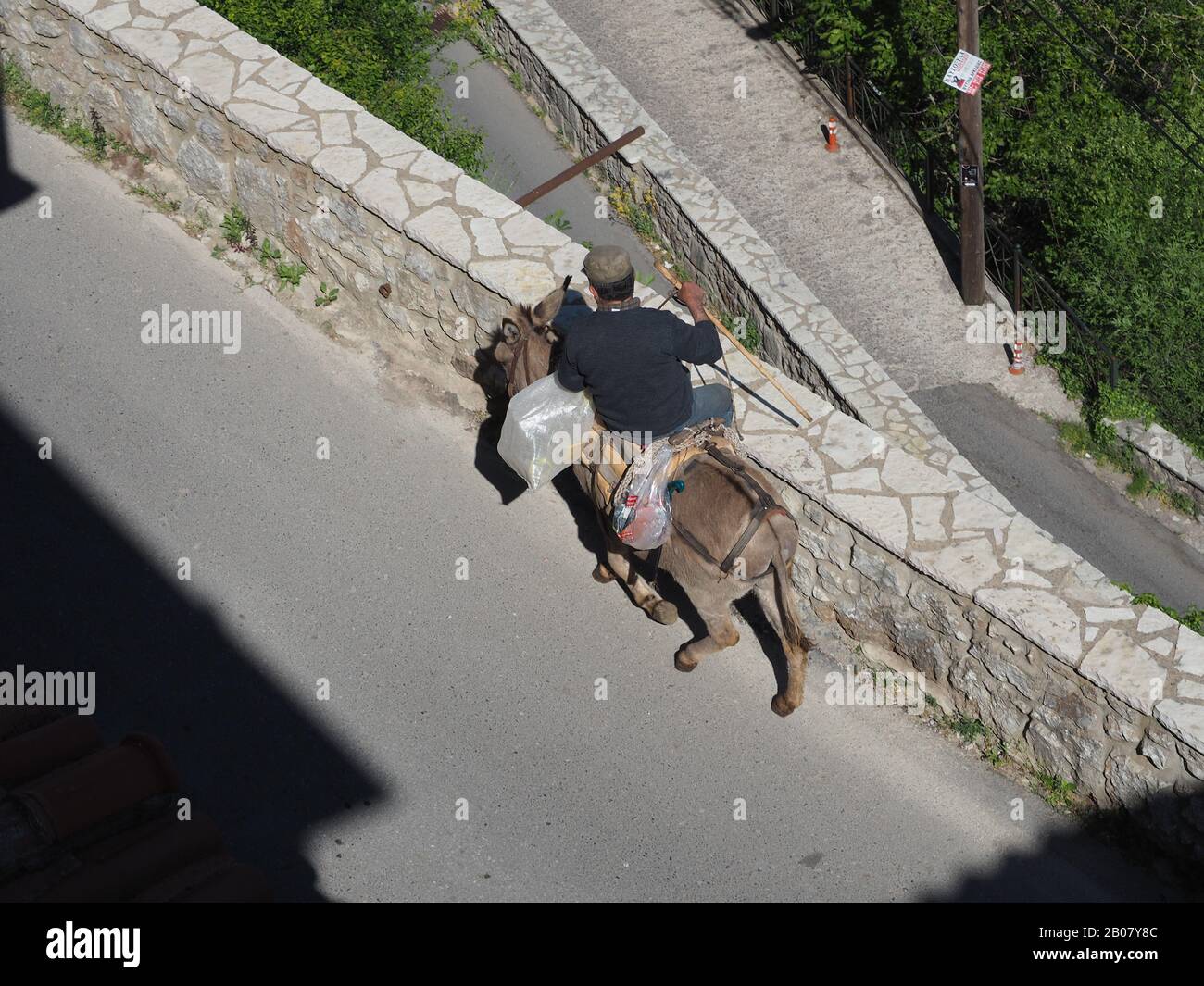 Uomo a cavallo asino che porta il suo shopping attraverso le strade di Dimitsana, Arcadia, Peloponneso, Grecia Foto Stock