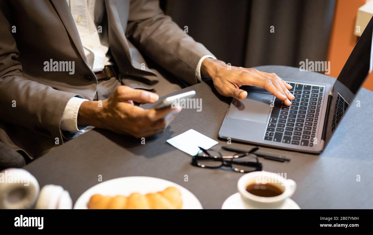 Immagine ritagliata di afro guy usando telefono e computer Foto Stock