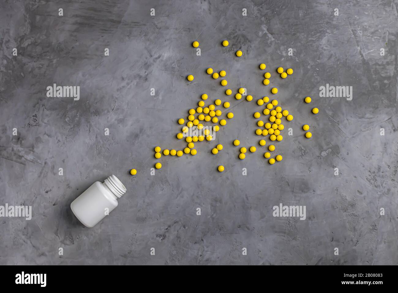 Vitamine gialle versate da una lattina bianca su fondo grigio in cemento. Draghi Di Vitamine Gialle. Foto Stock
