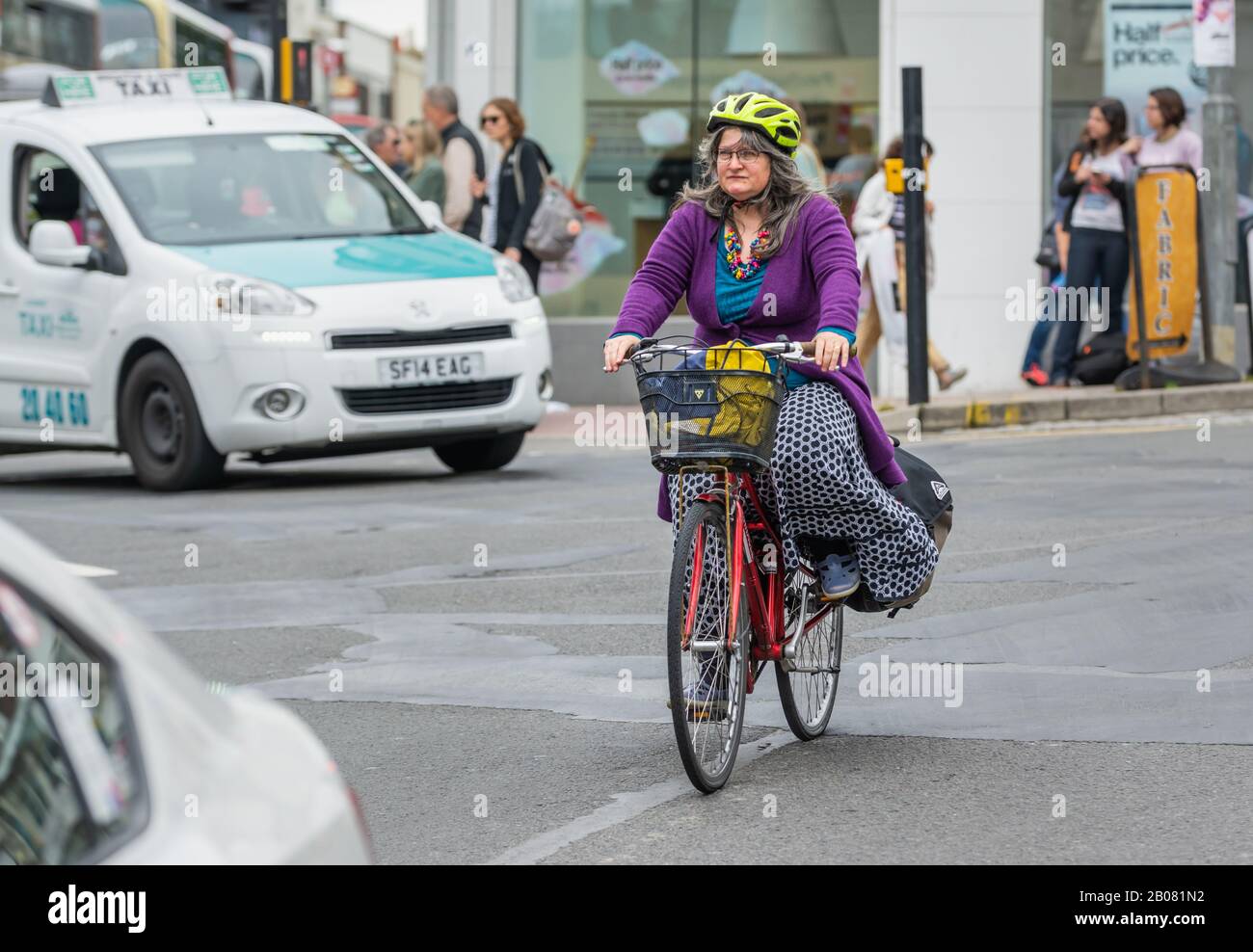 Una donna di mezza età che indossa un casco che guida una bicicletta su una strada nella trafficata città di Brighton, Inghilterra, Regno Unito. Donna in bicicletta. Foto Stock