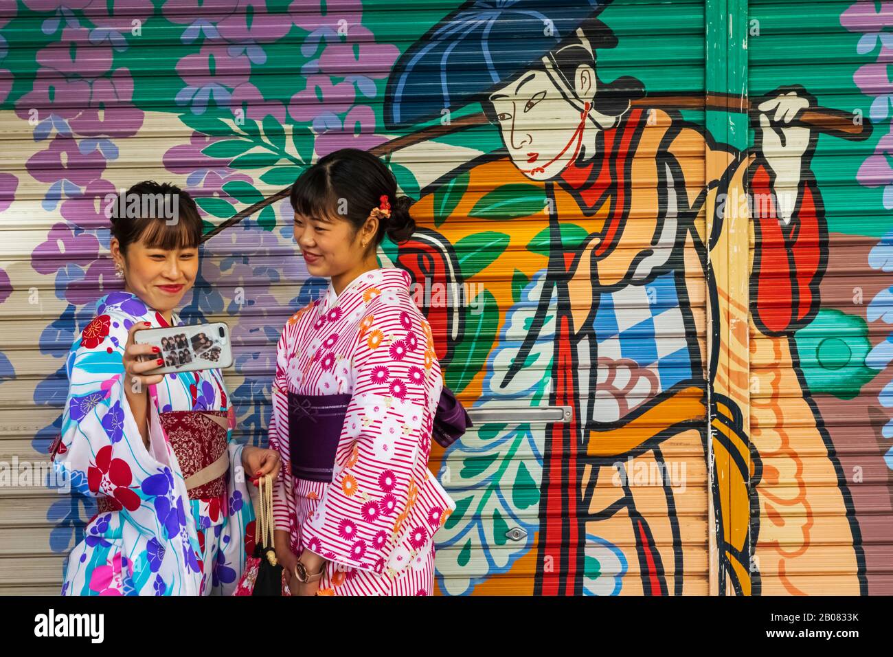 Giappone, Honshu, Tokyo, Asakusa, Due Donne In Kimono Scattare Foto Di Selfie Di Fronte Alla Coloratissima Pittura Dell'Otturatore Del Negozio Foto Stock