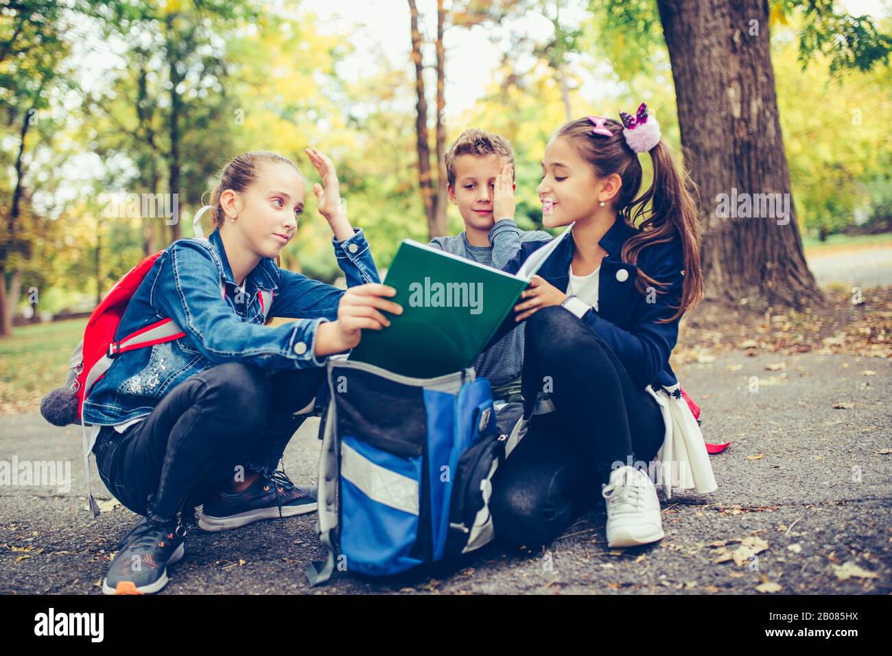 Ritorno a scuola. I bambini con gli zaini stanno avendo divertimento, parlando, leggendo un libro.Gruppo degli allievi elementari che hanno discusso dei compiti mentre vanno Foto Stock
