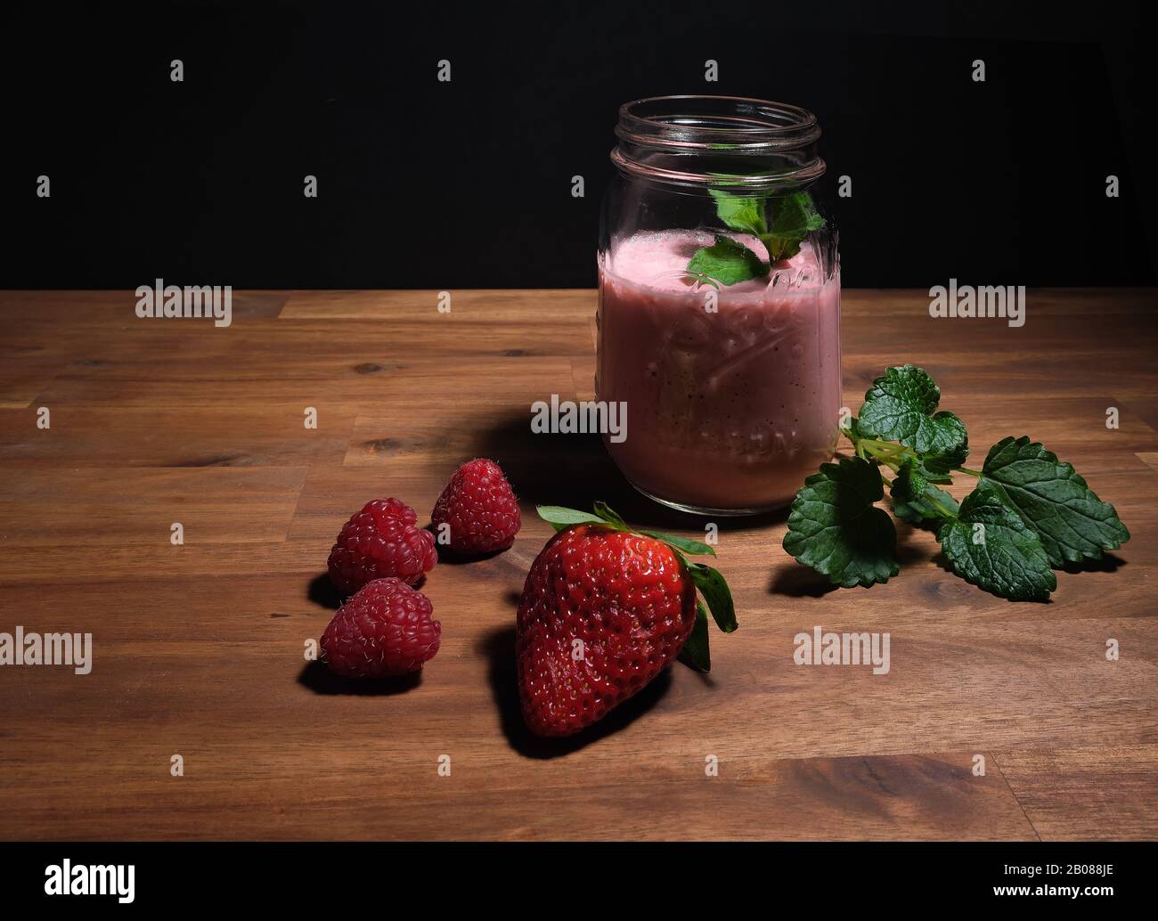 frullato di fragola disposto su un piatto di legno con sfondo nero, spazio pubblicitario Foto Stock