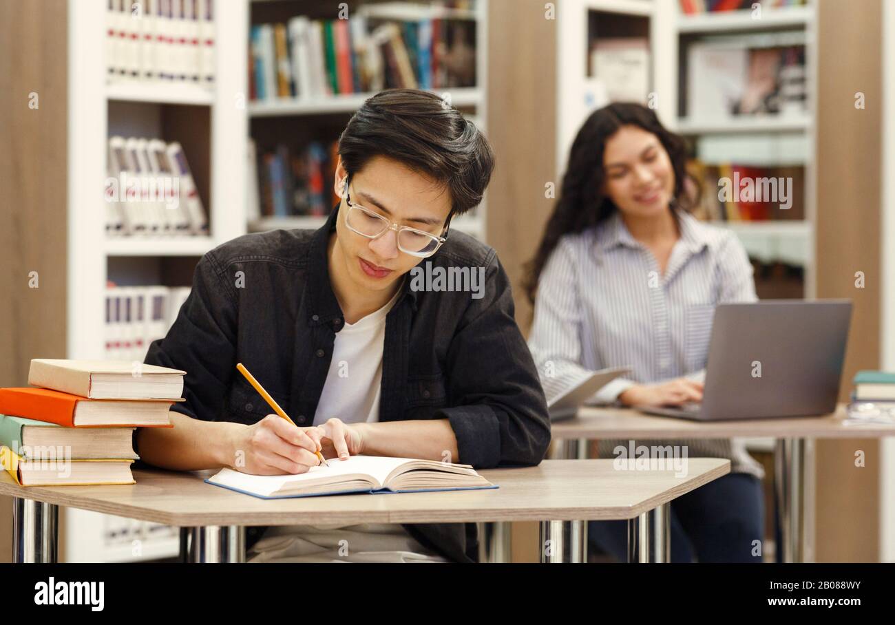 Ragazzo asiatico che fa ricerca seduto alla scrivania in biblioteca Foto Stock