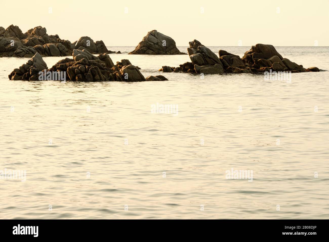 Rocce illuminate lateralmente dalla luce naturale in mare calmo Foto Stock