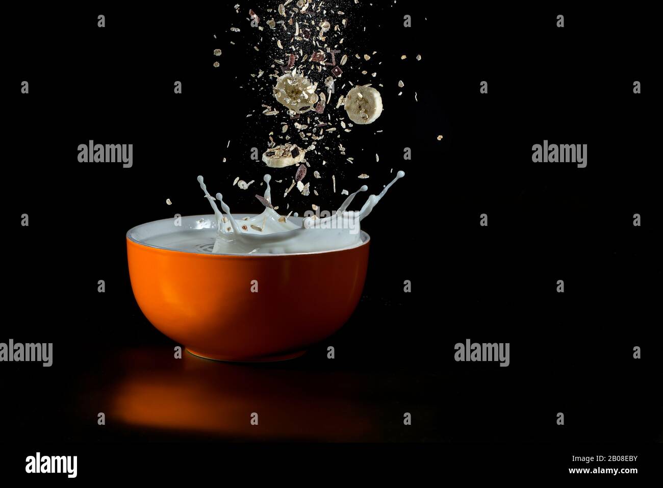 cereali che si levitano cadendo in una ciotola rossa con il latte schizzato - immagine ad alta velocità isolata su fondo nero Foto Stock
