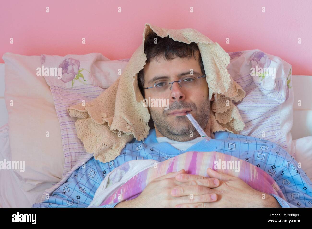 Ritratto di un giovane malato sdraiato a letto che prende la temperatura e ha l'influenza. Foto Stock