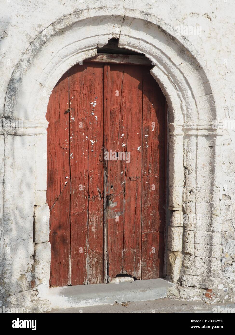 Vecchia porta in legno usurata, costellata di perni colorati in Kythira, Grecia, con arco in pietra. Foto Stock