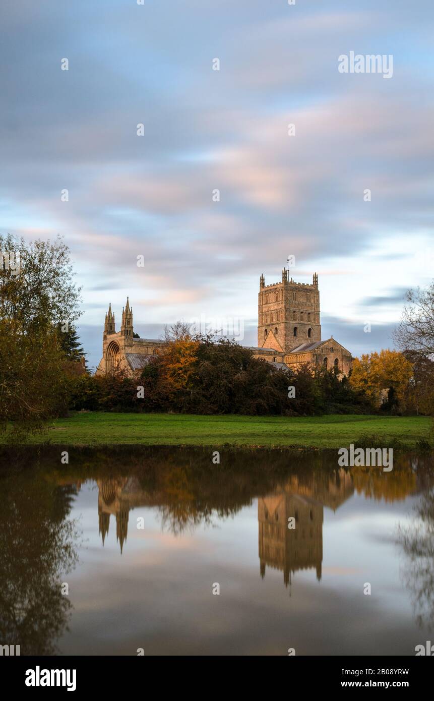 Abbazia di Tewkesbury, nel Worcestershire illuminata dal sole che tramonta all'ora d'oro durante e riflettendo nell'acqua delle inondazioni del 2019 Foto Stock