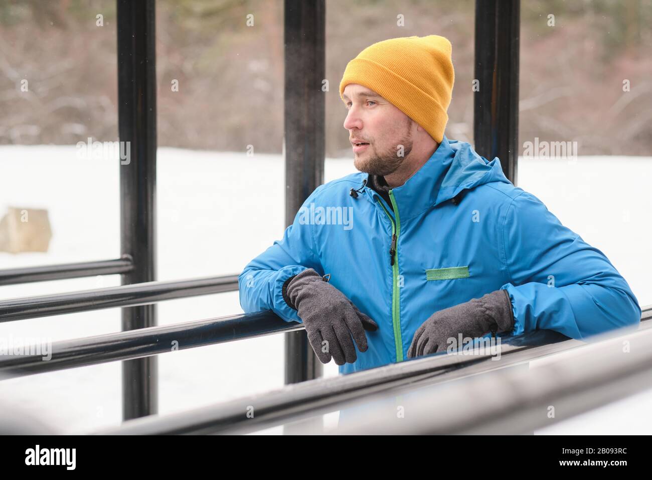 Giovane uomo contemplativo con spalle stoppie appoggiate su sbarre parallele mentre riposate dopo l'esercizio invernale Foto Stock