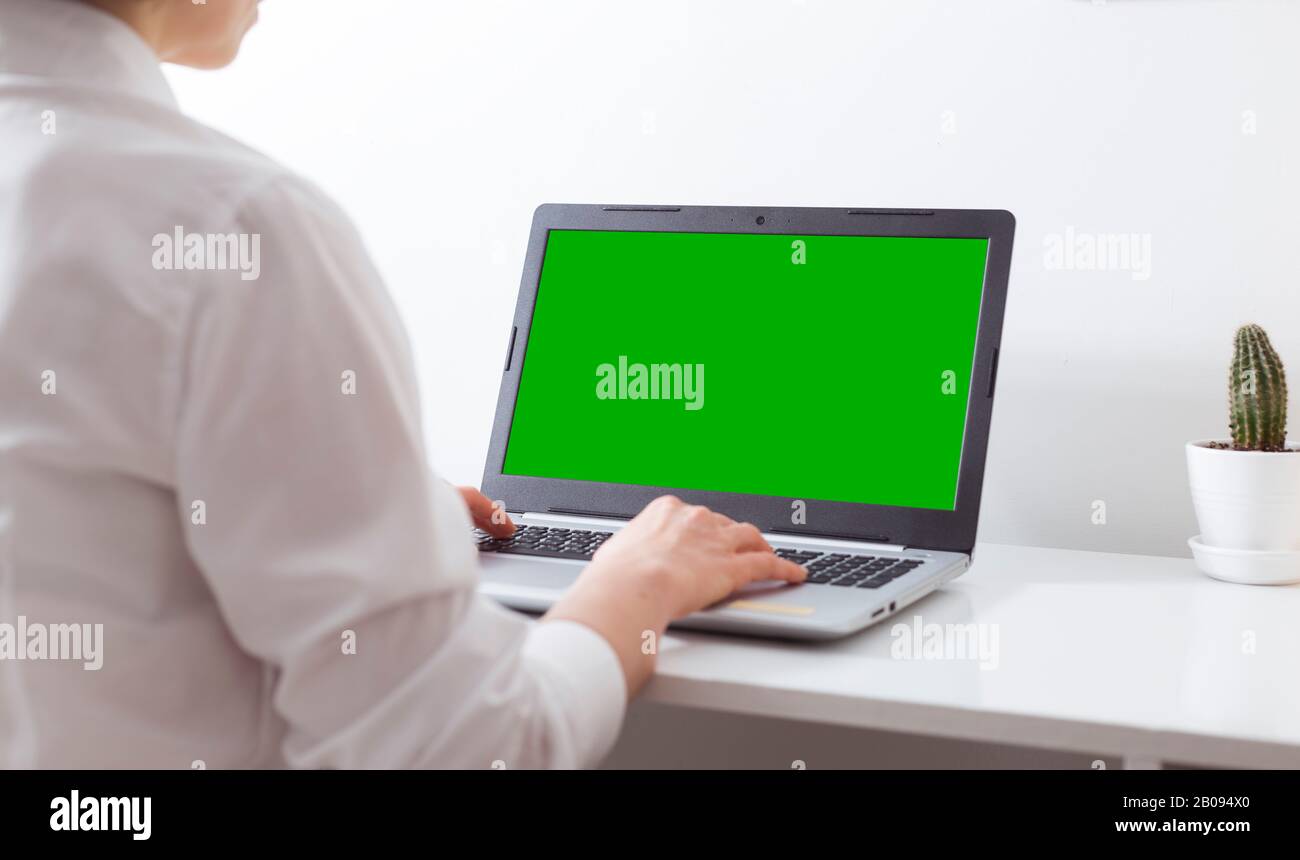 Una donna lavora in un ufficio bianco in un computer portatile con uno schermo verde. Foto Stock