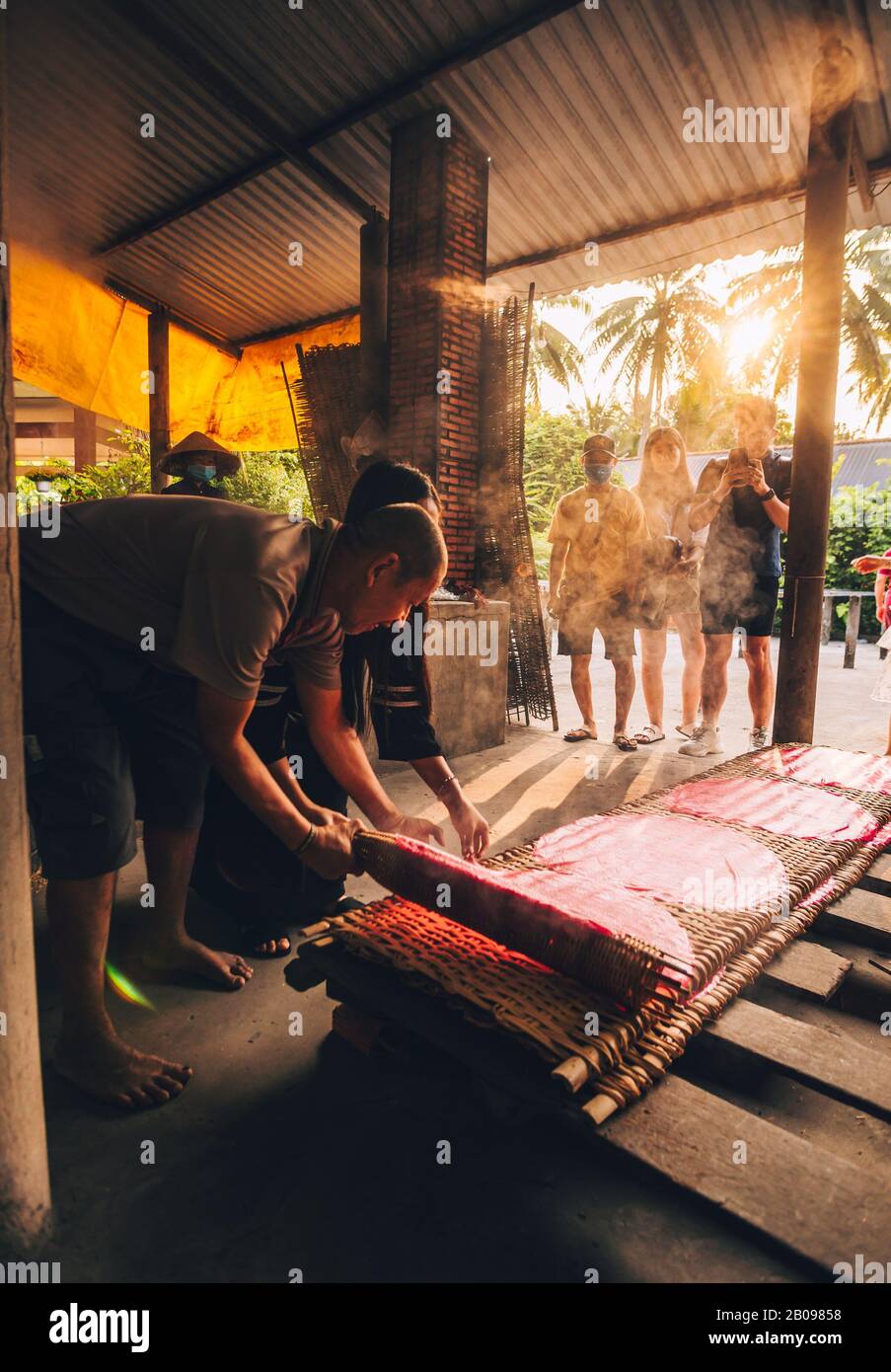 La gente del posto vietnamita alla fabbrica di Noodle mostra il processo di crearli. Riscaldare il liquido e delicatamente posandoli a riposare su fogli di bambù. Foto Stock