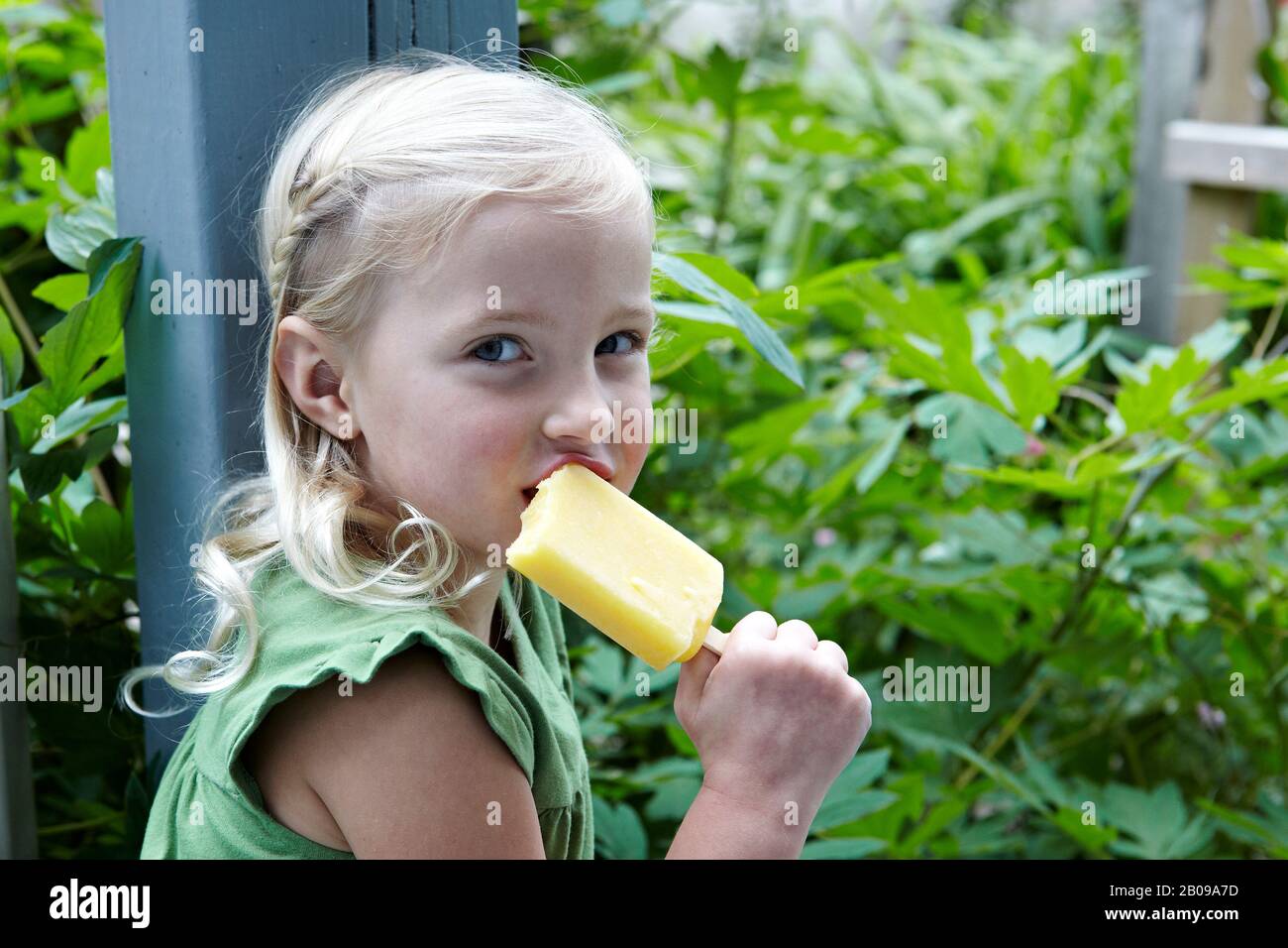 bella ragazza di 6 anni che mangia una poppicola di frutta nel suo giardino Foto Stock