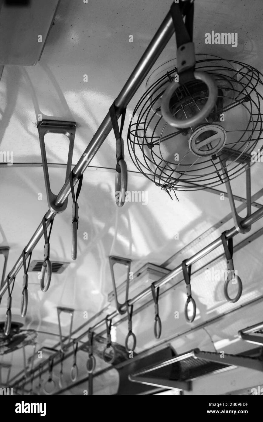 Viaggiare per conto proprio attraverso l'asia - Maniglie e ventilatore a soffitto per passeggeri in piedi all'interno di un treno Thailandia. Foto scattata in nero e con il whit Foto Stock