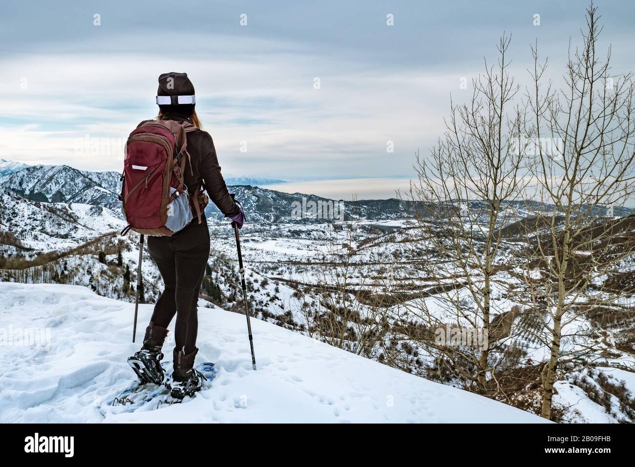 Hiker in montagna camminare su racchette da neve. La ragazza sul bordo della collina guarda in lontananza. Vista dal retro. Inverno turismo di montagna. Kazako Foto Stock