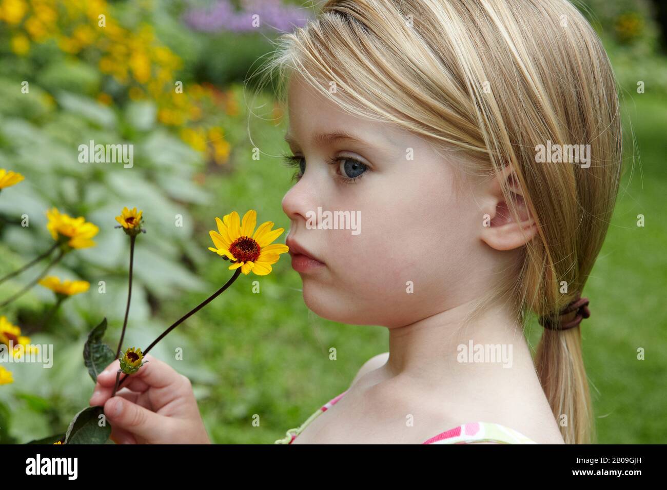 Profilo di bello 3 anni biondo toddler tenere e odorare un fiore giallo Foto Stock
