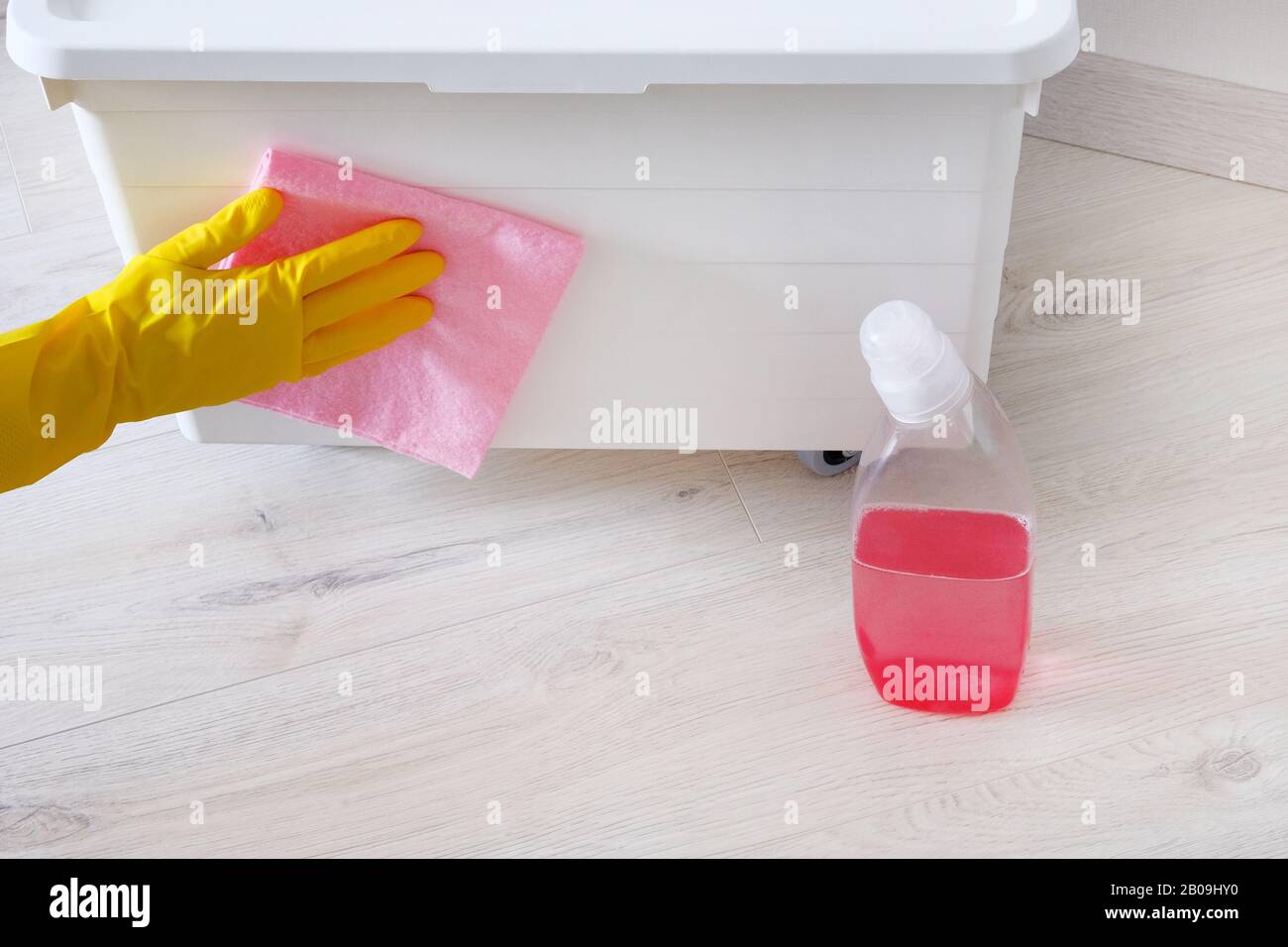 Concetto di pulizia in casa. Mano femmina in gomma gialla guanto protettivo panni scatola bianca con detergente rosa in camera. Il concetto di housework e housekeeping. Foto Stock