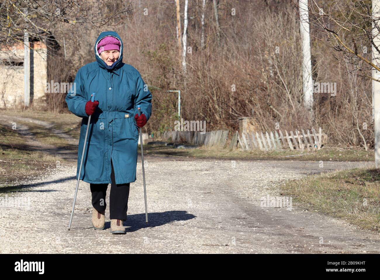 Donna anziana che cammina con bastoni sulla strada rurale, esercizi sportivi per la sana spina dorsale e articolazioni. Nordic walking a freddo, terapia per la salute Foto Stock