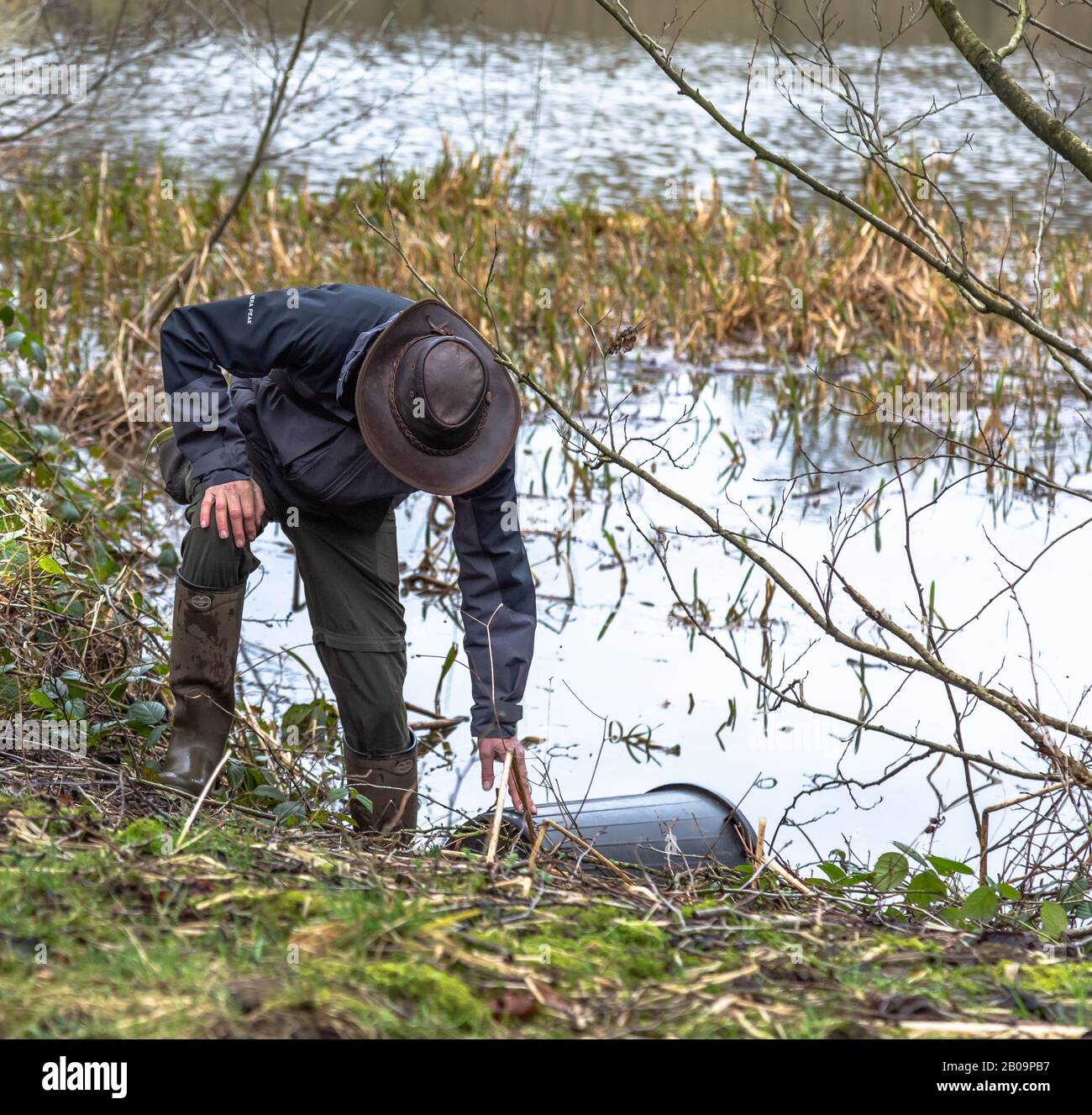 Un uomo recupera un contenitore di plastica che è soffiato in un lago. Foto Stock