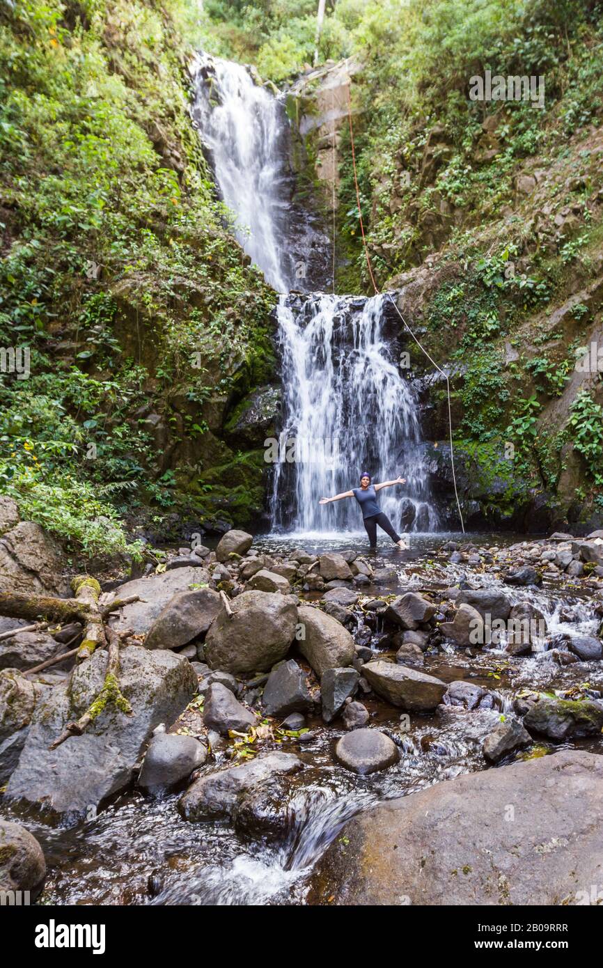 Donna locale che si trova alla base di una bella cascata nella foresta pluviale tropicale del Costa Rica Foto Stock