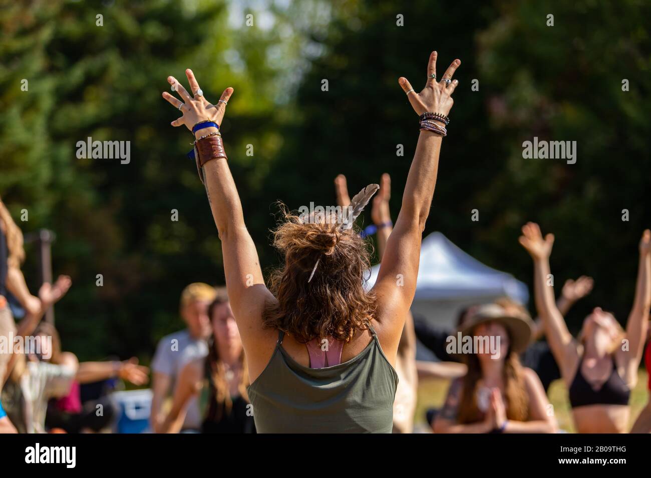 Una donna energica è vista guidare le persone attraverso una sessione di yoga e meditazione consapevole in natura, soft focus con gruppo sfocato in background Foto Stock