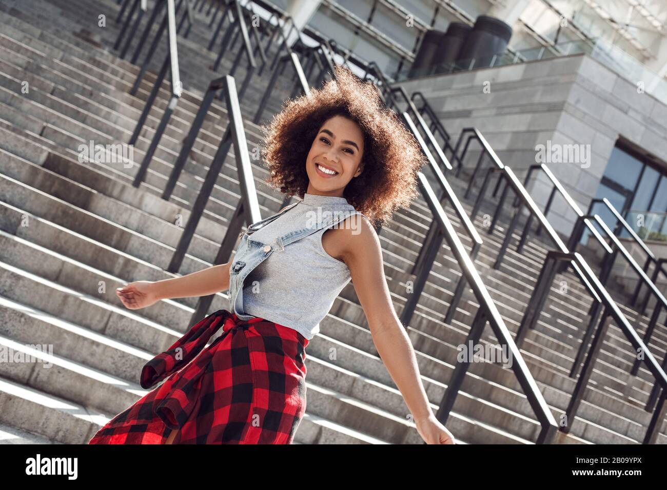 Giovane donna nella strada della città che si erge su scale sorridente allegro Foto Stock